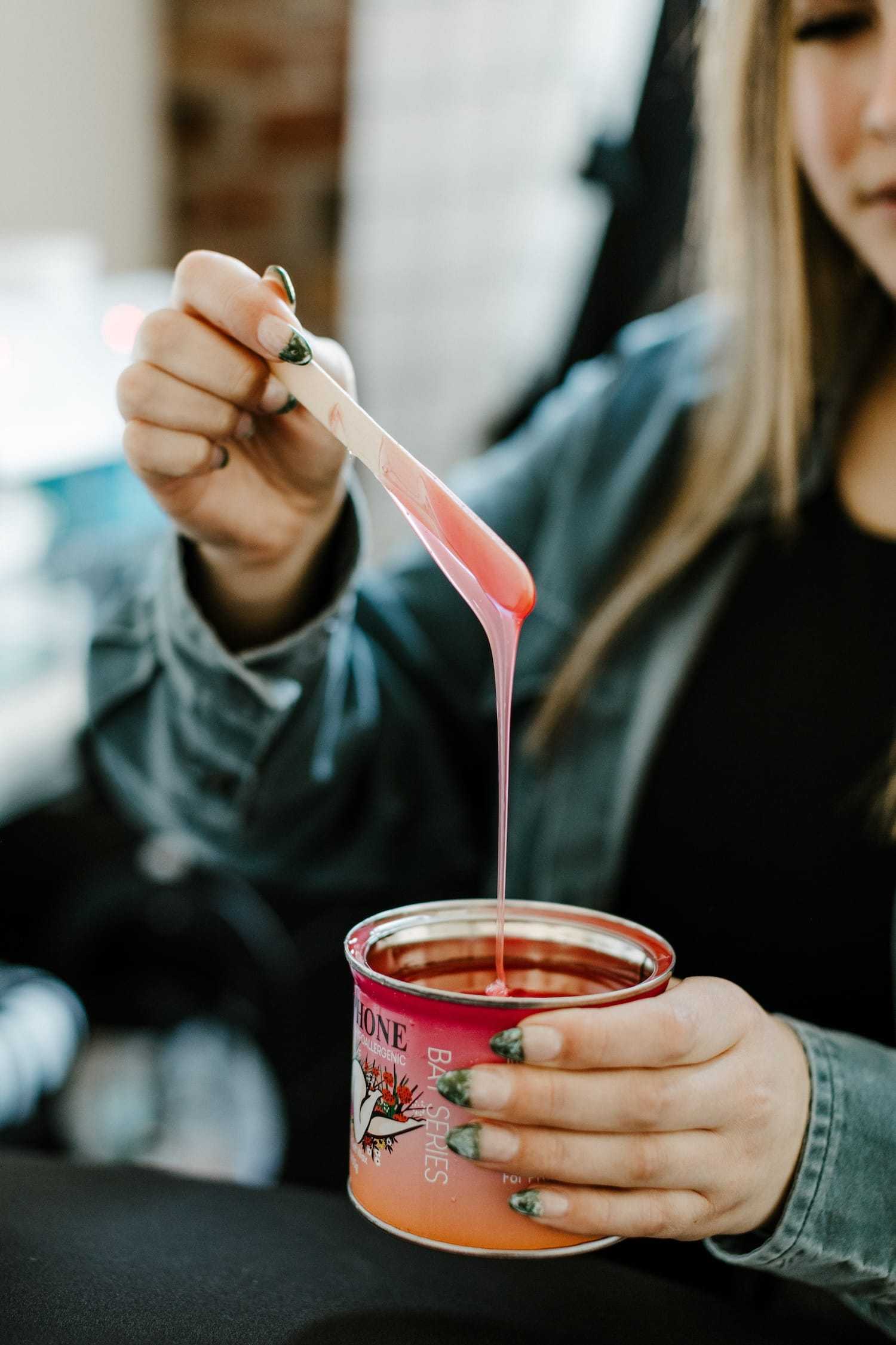 Person stirring a pink scented candle with a spatula.