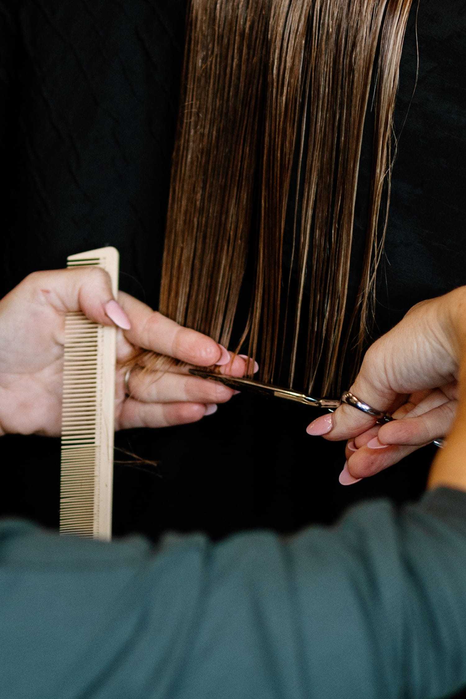 Hairdresser trimming ends of straight brown hair with scissors.