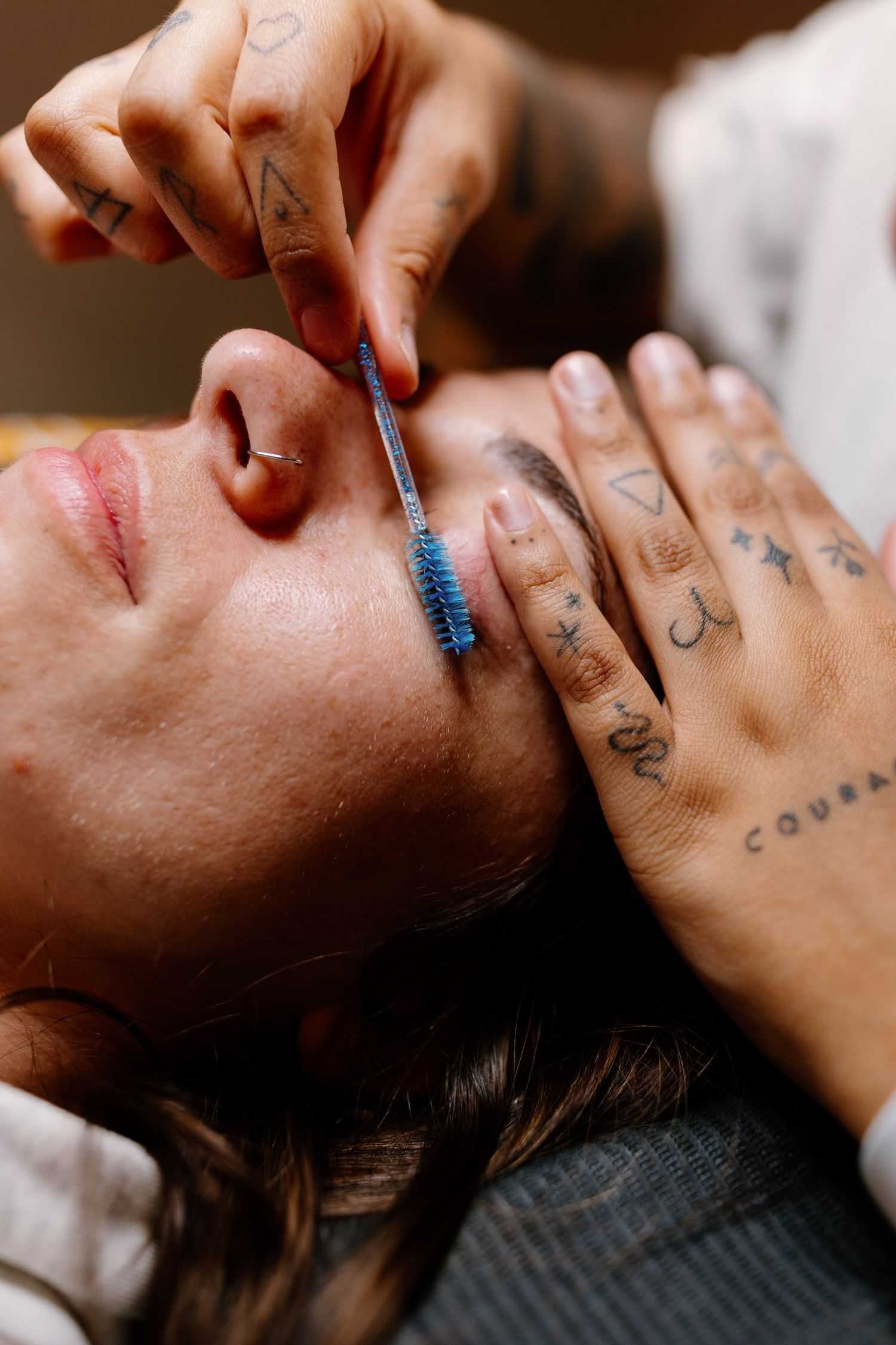 Person receiving an eyelash treatment with a brush tool.