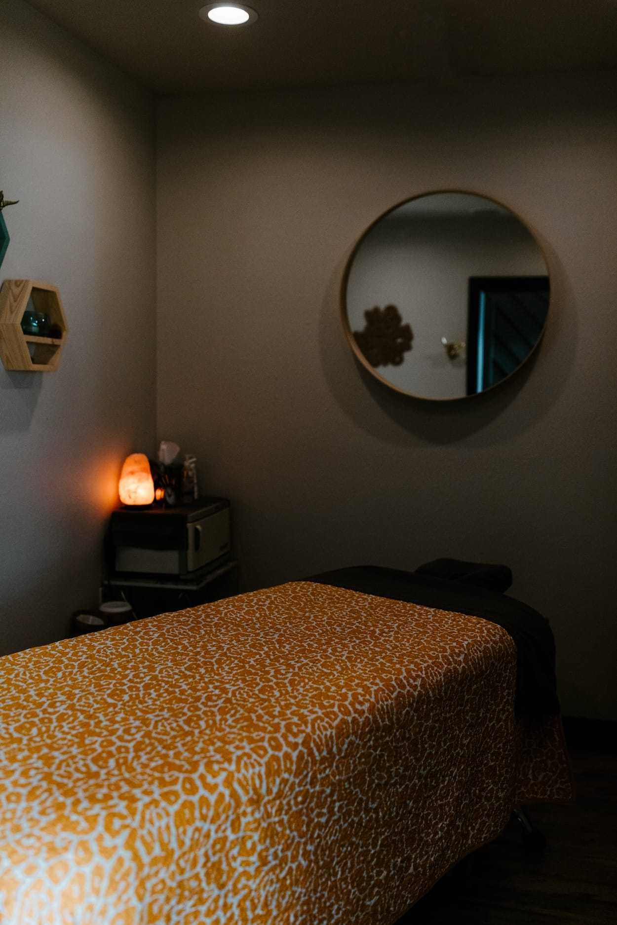 A cozy massage room with a leopard print bed cover and a round mirror.