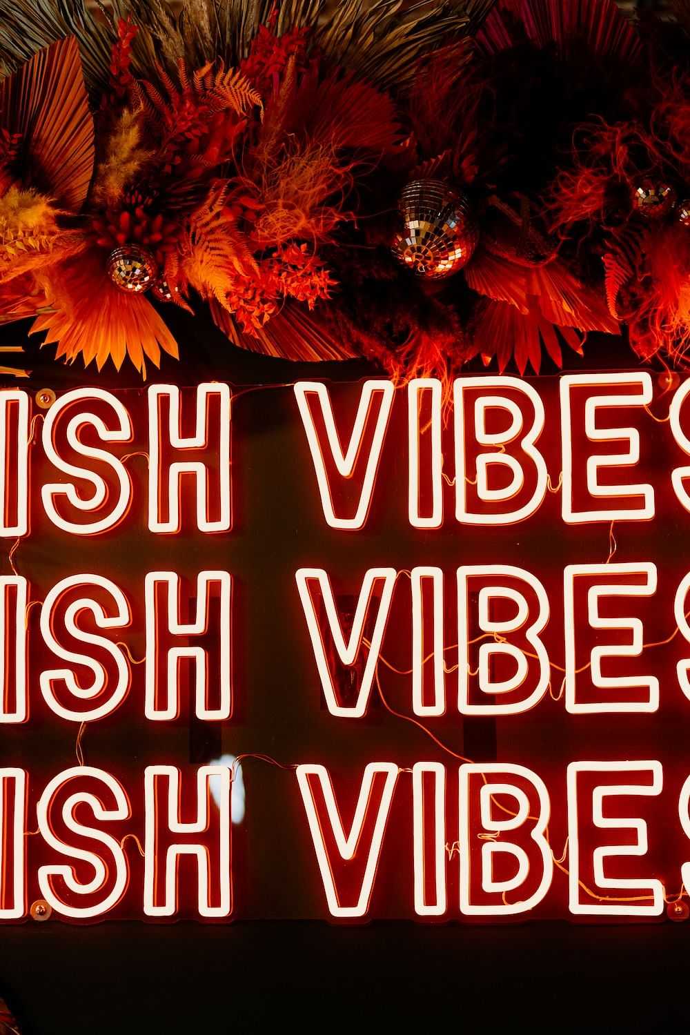 Neon sign reading "WISH VIBES" with floral decor in the background.